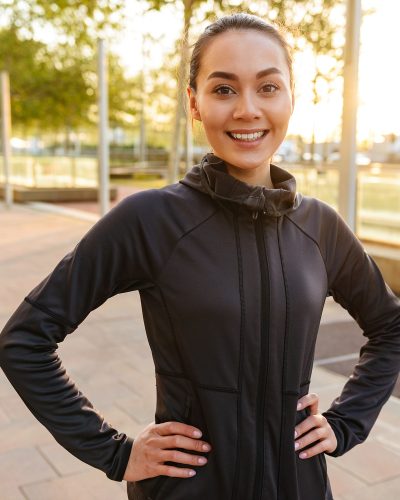 Picture of cheerful beautiful young asian sports woman looking camera outdoors.