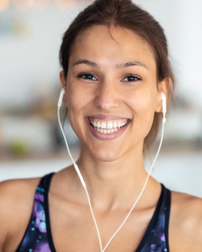 Portrait of smiling sporty woman listening to music after session of exercises in the kitchen at home.